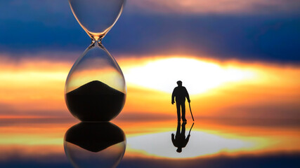 miniature people. silhouette of an elderly man walking towards the sunset next to an hourglass. end...