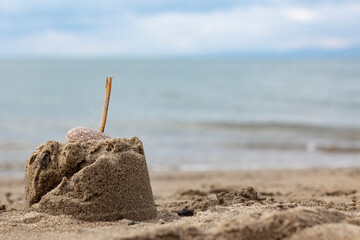 Mountain of sand with a wooden stick on beach seashore. Sandcastle with a stone on the beach. close-up of small sandcastles a stick topped with  against a blue sky