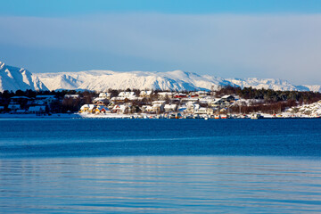 Small village located on sea coast in front of snowy mountains, Norway