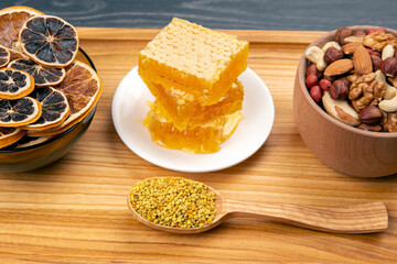 assortment of nuts and assorted dried citrus fruits and fresh floral honeycomb honey and pollen on kitchen wooden board. useful vitamin food for the human body