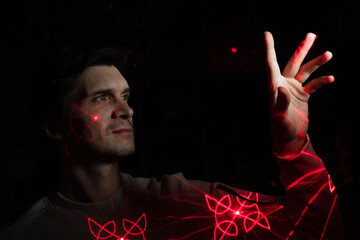 Interaction with augmented reality virtual interface, concept. A young man with projections of red patterns on his face pulls his hand forward