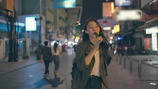Asian young woman traveler drink bottle of beer while walk on street. 