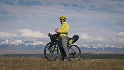 The man travel on mixed terrain cycle touring with bikepacking. The traveler journey with bicycle bags. Sport bikepacking, bike, sportswear in green black colors. Mountain snow capped, stone arch.