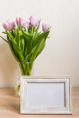 Portrait white picture frame mockup on wooden table. Modern vase with tulips.Scandinavian interior