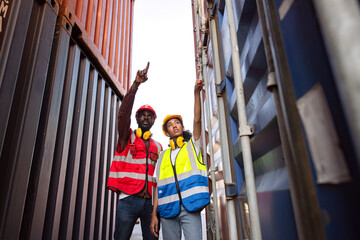 Two African american male and female worker check and control loading freight containers from Cargo freight ship for import export.
