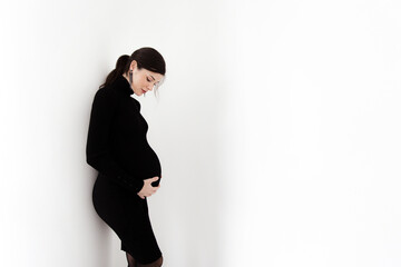 Pregnant brunette in a black dress with a neck on a white background