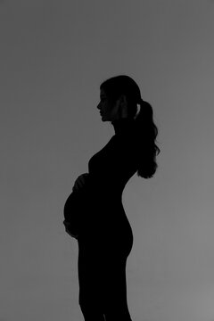 Silhouette of a pregnant girl in a black dress in a photo studio