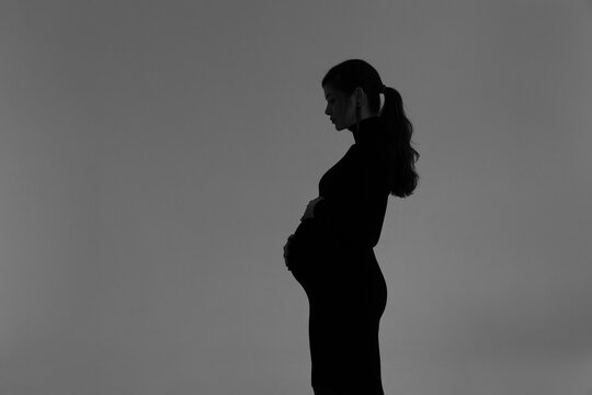 Silhouette of a pregnant girl in a black dress in a photo studio