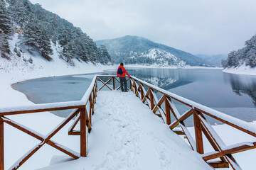 cold winter season and man in red coat looks at the lake. Sunnet lake
