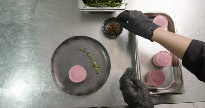 hands add decorations to a small round pink dessert from the restaurant kitchen to serve fresh vegan cuisine, rav dessert vegetriano, natural, vegetable food, plants, macro close-up shot
