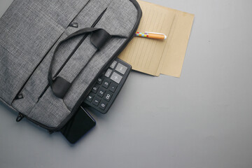 Top view of note pad, calculator, pen in a office bag on gray background 