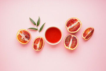 Halves of blood oranges and glass of blood orange juice on a pink background. Top view.