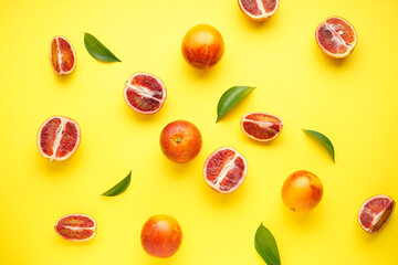 Ripe blood oranges sliced and whole with sprigs of green leaves on a yellow background. Top view.