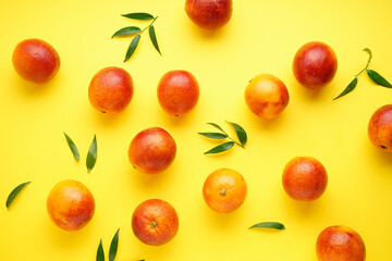 Blood oranges with sprigs of green leaves on a yellow background, flat lay.