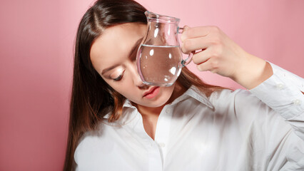 A beautiful young brunette holds a glass of clean water in her hands, the benefits of clean water for beauty and health, concept. Parts of the face are refracted in a glass of water