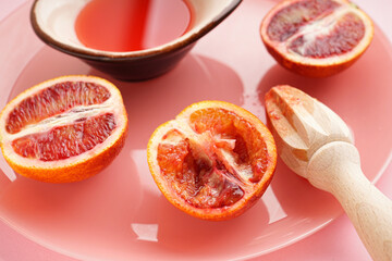 Blood oranges and a wooden juicer with of blood orange juice on a pink background. Close-up