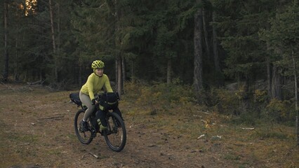 Naklejka premium The woman travel on mixed terrain cycle touring with bike bikepacking outdoor. The traveler journey with bicycle bags. Stylish bikepacking, bike, sportswear in green black colors. Magic forest park.