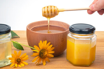 fresh floral honey dripping from a spoon into a wooden plate on a white background. organic vitamin...
