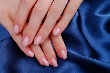 The hands of a young girl on a blue silk fabric, pink nail polish.The concept of hand care,...
