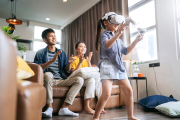 exiting daugther wear vr headset playing virtual gaming sport innovation while her parent sit and cheering together on sofa counh living room at home,asian family spending fun moment weekend activity