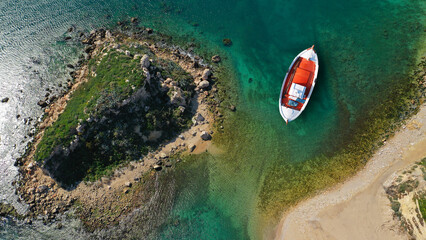 Aerial top view photo of red traditional wooden fishing boat anchored in Aegean island destination port with emerald sea