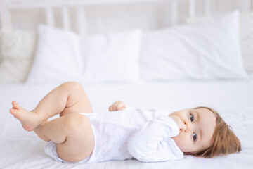 funny baby girl of six months on a bed in white clothes smiling, a small child on a cotton bed at home woke up in the morning after sleeping, the concept of children's goods