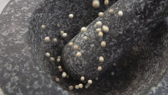Spicy grey peppercorns are falling and bouncing into the grey stone mortar