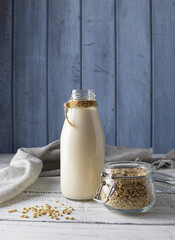 Barley milk in a glass bottle on white wooden boards. Barley grains in a transparent jar. Blue boards in the background
