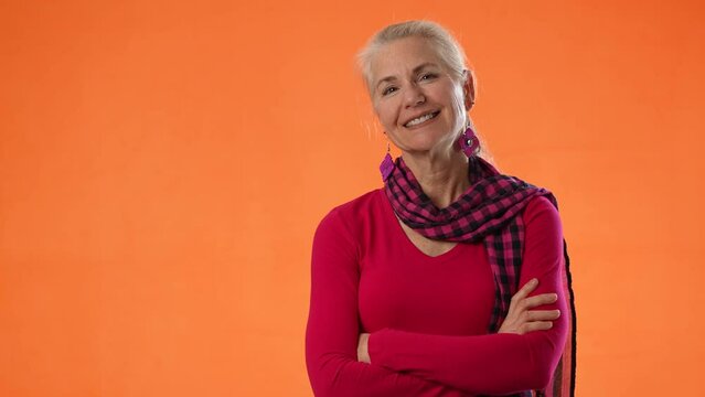 Portrait of beautiful smiling mature woman crossing arms on orange color background, with copy space for product or sale.