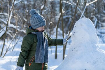 little boy in a grey hat is making a snowman.