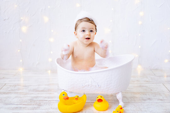 a joyful baby girl of six months is bathing in a bath with foam and rubber ducks, a small child is having fun playing with water, the concept of care and hygiene