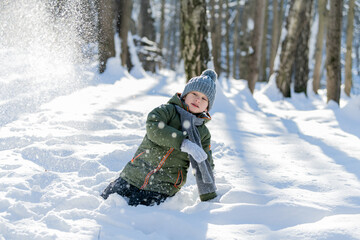 Fototapeta na wymiar little boy throwing snow in the woods in winter