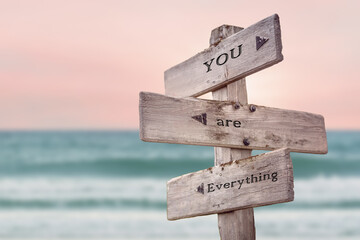 you are everything text quote written on wooden signpost by the sea. Positive pink turqoise pastel theme.