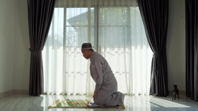 An elderly Muslim man with a gray beard prays at home during the coronavirus pandemic. Covid-19, quarantine concept	