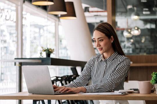 Attractive Asian Woman Using Laptop While Doing Homework Making Video Call Abroad Using Internet Friend Connection, Business Women Use Computer Analysis Finance Data