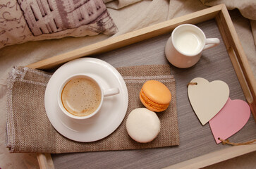 Morning coffee with milk and macarons on a tray in bed