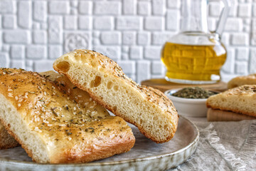 Freshly baked Italian traditional homemade focaccia on a light background. Focaccia bread sliced with olive oil and basil.