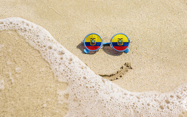Sunglasses with flag of Ecuador on a sandy beach. Nearby is a sea lightning and a painted smile. The concept of a successful vacation in the resorts of Ecuador.