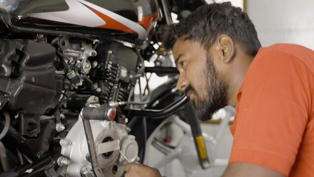 handheld shot of exhausted bike mechanic fixing or reparing engine of motorbike at garage ueing tools - concept of Hard working, maintenance service and occupation.