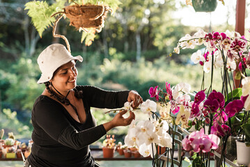Very cheerful Latina woman taking care of the orchid plants in the greenhouse. 