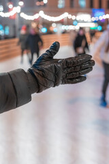 Outstretched hand in a leather black glove against the background of people skating (1196)