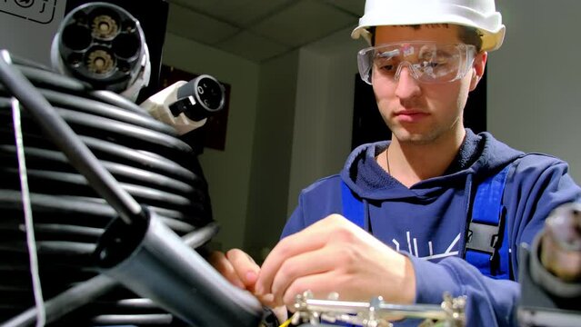 Foreman in goggles deals with wires developing plug cable for charging ev with alternative energy. Portable charging station assembling close view
