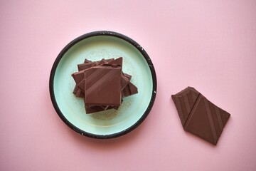 tabliczki czekolady na niebieskim talerzyku na różowym tle 