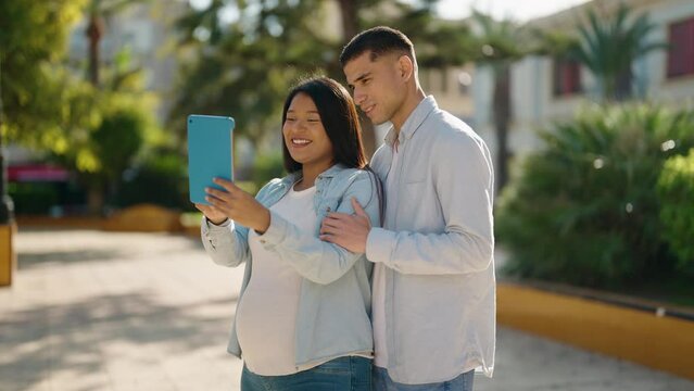 Young latin couple hugging each other using touchpad at park
