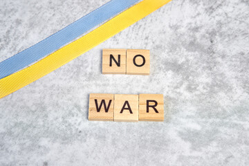 phrase no war is laid out of wooden squares on a gray background with flag of ukraine with blue and yellow ribbon. Concept of peace, war in Ukraine