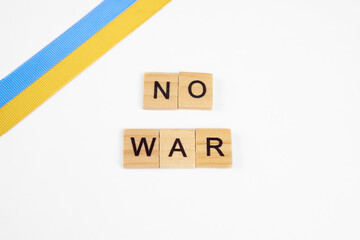 phrase no war is laid out of wooden squares isolated on white background. with flag of ukraine with blue and yellow ribbon. Concept of peace, war in Ukraine