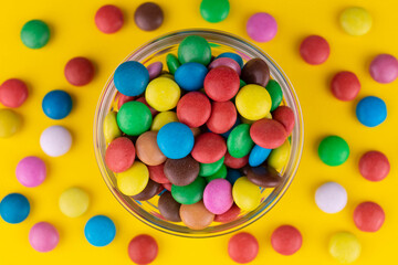 Small multi-colored sweets in a bowl on a yellow background.