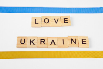 phrase love ukraine is laid out of wooden squares isolated on white background. with flag of ukraine with blue and yellow ribbon. Concept of peace, war in Ukraine