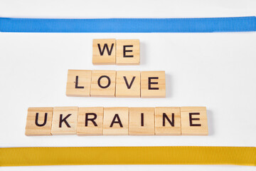 phrase we love ukraine is laid out of wooden squares isolated on white background. with flag of ukraine with blue and yellow ribbon. Concept of peace, war in Ukraine