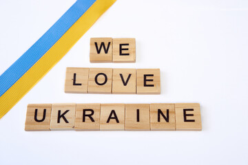 phrase we love ukraine is laid out of wooden squares isolated on white background. with flag of ukraine with blue and yellow ribbon. Concept of peace, war in Ukraine